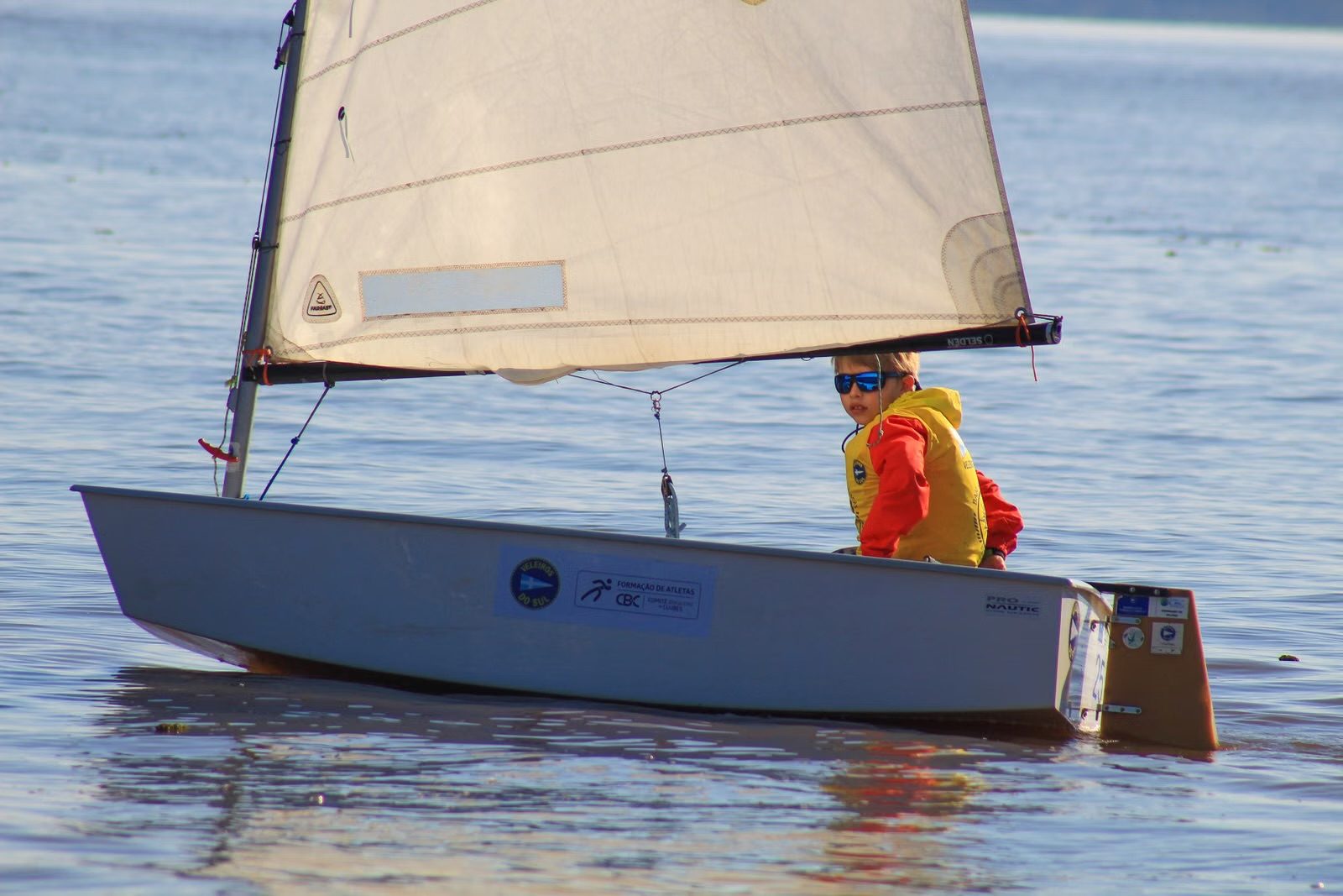 Un jeune marin seul à la barre de son petit voilier